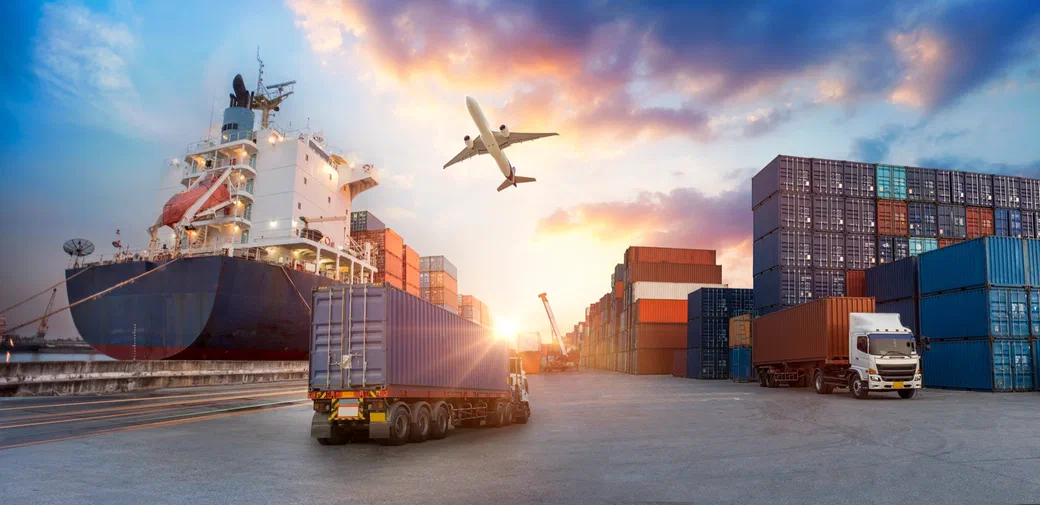 A container ship, cargo plane, and truck at a port at sunset